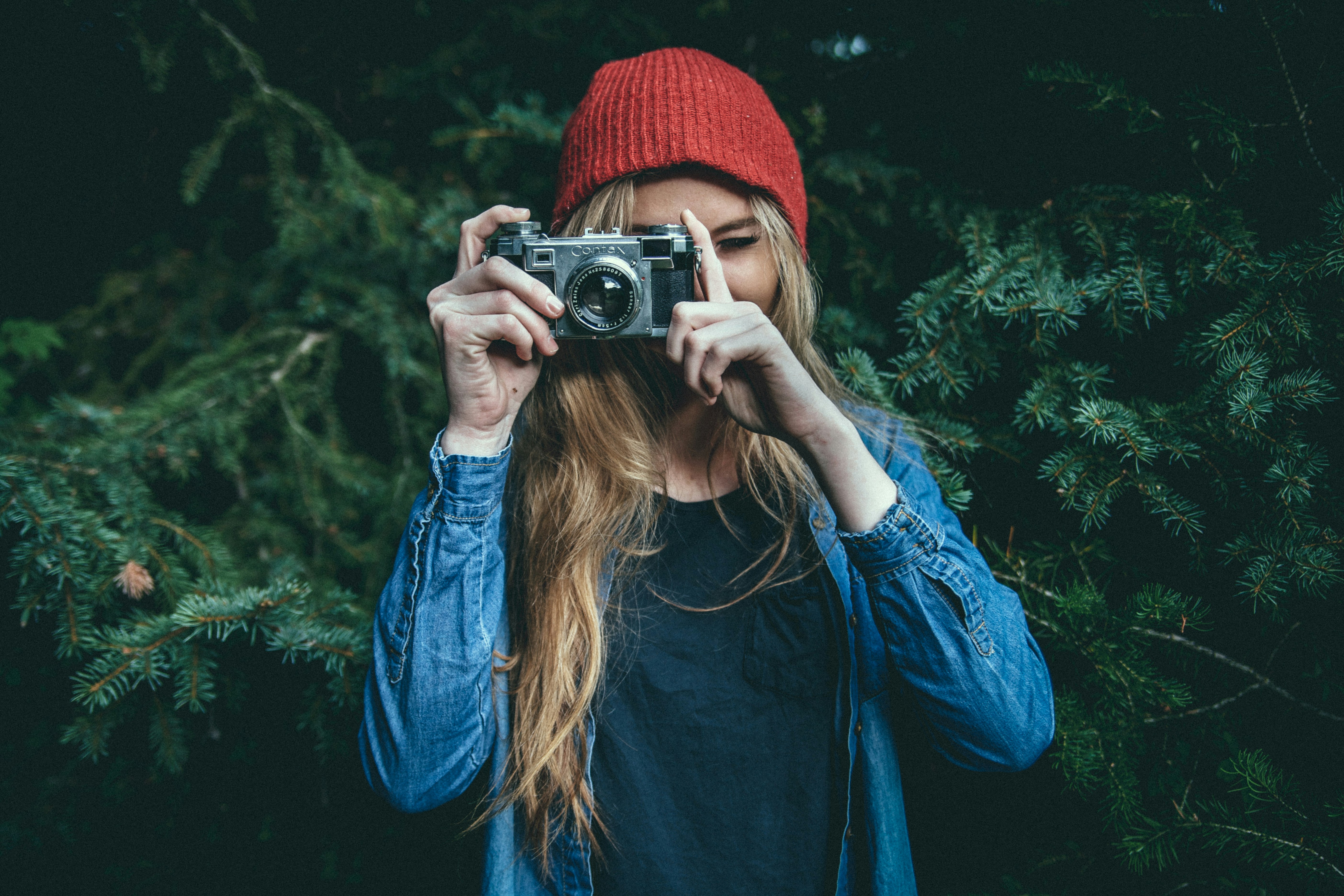 woman standing behind green leaf tree holding DSLR camera